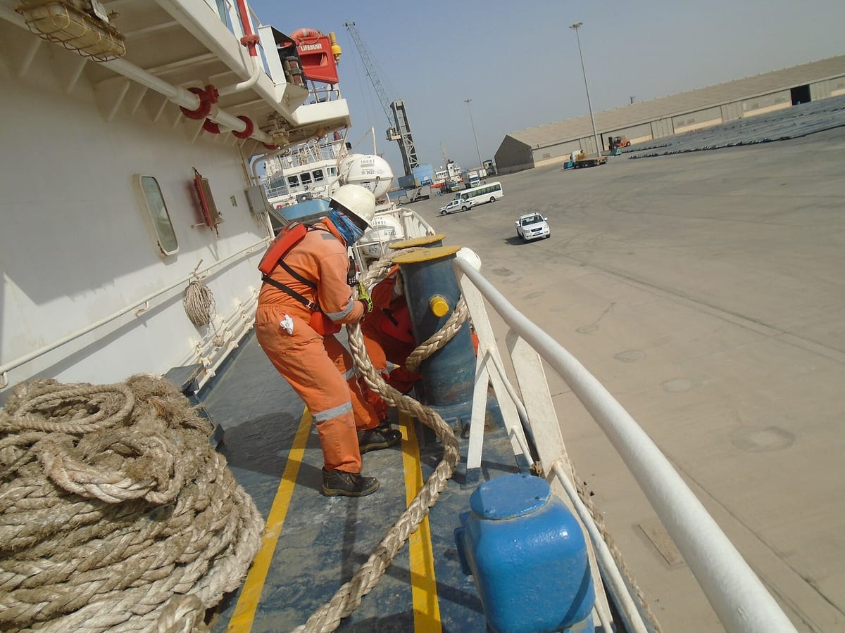 Deck crew in orange coveralls securing a mooring rope to a bollard